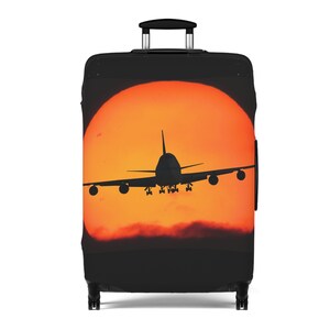May include: Black suitcase luggage cover with a silhouette of an airplane flying in front of an orange sunset.