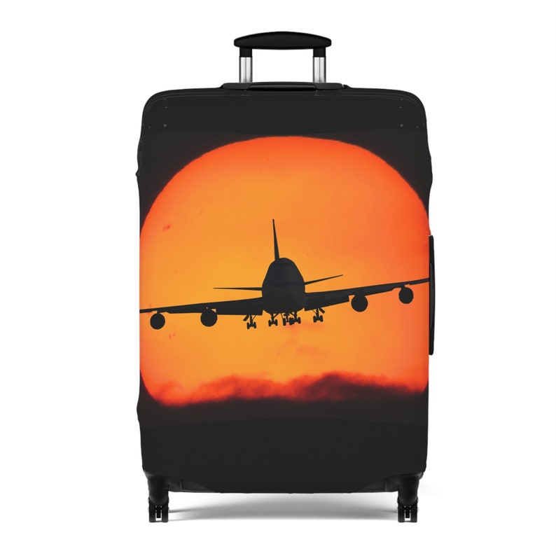 May include: Black suitcase luggage cover with a silhouette of an airplane flying in front of an orange sunset.