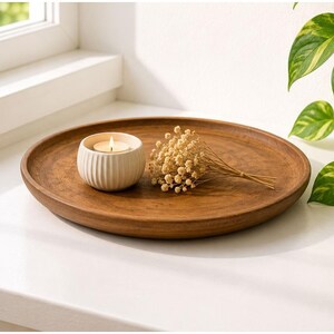 Peut inclure: Un plateau rond en bois brun contenant un petit bougeoir en céramique crème à côtes avec une bougie chauffe-plat allumée, accompagné d'un petit bouquet séché de fleurs de gypsophile beige clair posé sur la surface du plateau.