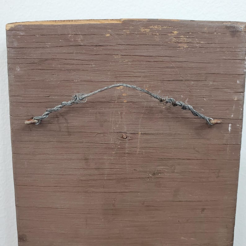 Puede incluir: Parte trasera de un letrero rectangular de madera con acabado marr&oacute;n. Se adjunta un alambre retorcido para colgarlo. La veta de la madera es visible y el letrero muestra signos de desgaste y edad.
