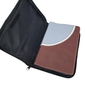 May include: A Bible in a black zippered case. The Bible has a two-tone cover, with a brown leather-like bottom and a light blue top section. A white and cream-colored curved accent separates the two colors.