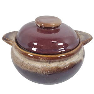 Peut inclure: Un petit plat à casserole rond en céramique avec couvercle. Le plat est de couleur bordeaux foncé avec un bord et des poignées marron clair. Le couvercle a un petit bouton arrondi. Idéal pour la cuisine et le service.