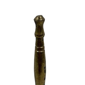 May include: A vertical brass rod featuring a tapered, cylindrical body with a rounded, knob-like top. The metal surface displays a weathered, aged patina with visible dark spots and horizontal grooves along the upper section of the shaft.