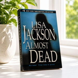 May include: A hardcover book titled "Almost Dead" by Lisa Jackson. The cover features a silhouette on a blue background. The text reads "#1 New York Times Bestselling Author" and "All new! First time in print!"