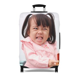 May include: A white suitcase with a colorful image of a young girl with pigtails. The girl is wearing a pink and white striped shirt and has a playful expression on her face.