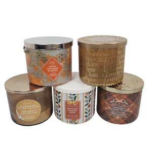 Pode incluir: Cinco velas perfumadas com tampas metálicas. As velas têm rótulos com textos como "Sweet Cinnamon Pumpkin", "Cinnamon Spiced Vanilla" e "Cinnamon Sugared Pecans". Os recipientes das velas são de várias cores.