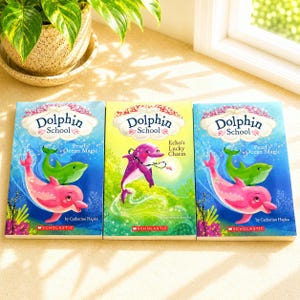 Peut inclure: Trois livres pour enfants intitulés "Dolphin School" sont présentés. Les couvertures présentent des illustrations colorées de dauphins dans un cadre sous-marin. Les livres sont "Pearl's Ocean Magic" et "Echo's Lucky Charm" par Catherine Hapka.