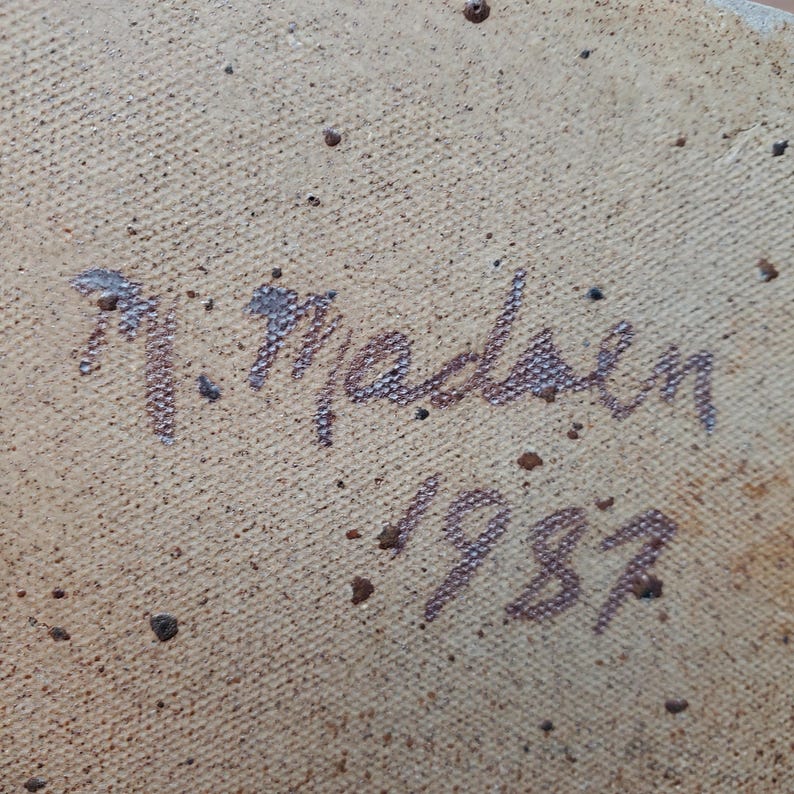 K&ouml;nnte beinhalten: Nahaufnahme einer strukturierten, beigefarbenen Oberfl&auml;che mit der handschriftlichen Signatur "N. Madsen" und dem Jahr "1987" in Dunkelbraun. Die Oberfl&auml;che hat kleine, dunkelbraune Sprenkel.