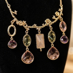 Könnte beinhalten: Eine goldfarbene Halskette mit floralem Rankendesign. Die Halskette verfügt über verschiedene Edelsteinanhänger in Rosa-, Grün- und Lilatönen. Die Edelsteine haben ovale, tropfenförmige und rechteckige Formen und sind an der Ranke befestigt.