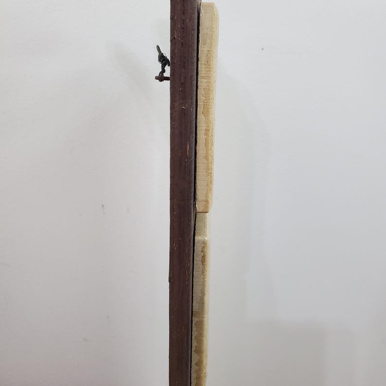 Puede incluir: Vista vertical de un marco de madera, con un borde marr&oacute;n oscuro y un panel de madera claro, posiblemente sin terminar. Una peque&ntilde;a bisagra met&aacute;lica oscura es visible en la parte superior. El marco est&aacute; contra un fondo blanco liso.