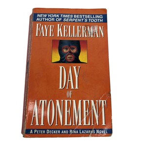 May include: A hardcover book titled "Day of Atonement" by Faye Kellerman. The cover is orange with the title in large white letters. A picture of a person wearing a black mask is in the center. The text "New York Times Bestselling Author" is at the top.