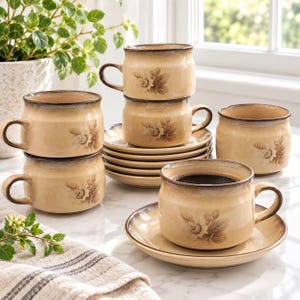 May include: A set of ceramic cups and saucers in a light beige glaze with a darker brown gradient rim. Each piece features a brown floral botanical illustration. The set includes four cups with handles and a stack of matching saucers on a surface.