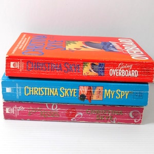 May include: Three paperback books stacked on top of each other. The top book is red with the title "Going Overboard" and the author's name "Christina Skye". The middle book is blue with the title "My Spy". The bottom book is pink.