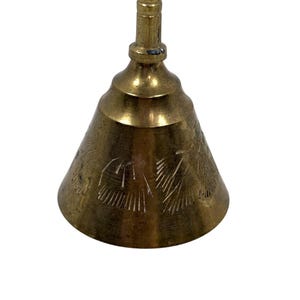 May include: A vintage brass bell with a conical shape and a long handle. The bell has etched floral designs on its surface. The bell is a warm gold color and is set against a white background.