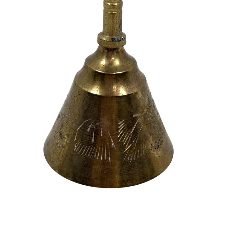 May include: A vintage brass bell with a conical shape and a long handle. The bell has etched floral designs on its surface. The bell is a warm gold color and is set against a white background.