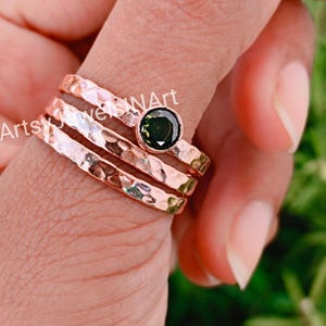 May include: Three hammered rose gold rings with a dark green gemstone set in the centre ring.