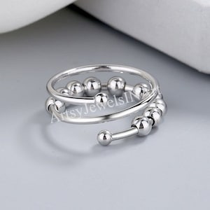 May include: A silver ring with a double band of small, round beads. The beads are arranged in a spiral pattern.