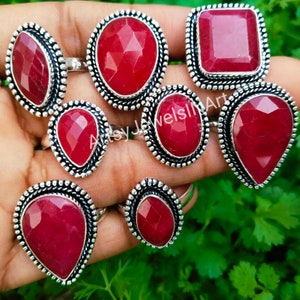 Op de afbeelding: Een set van acht zilveren ringen met rode edelsteen bezettingen. De ringen hebben verschillende stijlen, waaronder ovale, vierkante en druppelvormen. De edelstenen zijn diep rood van kleur en hebben een facetgeslepen.