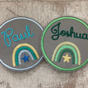 Könnte beinhalten: Zwei graue und grüne gestickte Patches mit Regenbogen-Designs und einem Stern. Die Patches sind rund und haben die Namen "Paul" und "Joshua" gestickt.