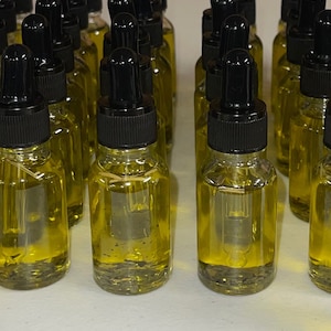 May include: A group of 15 small glass bottles with black dropper tops filled with a clear yellow liquid. The bottles are arranged in rows on a white surface.