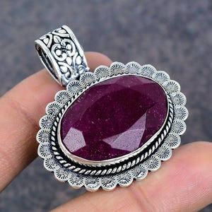 May include: A silver pendant featuring an oval ruby gemstone set within an intricate silver frame. The pendant boasts a floral design and is ideal for adding a touch of elegance to any outfit.