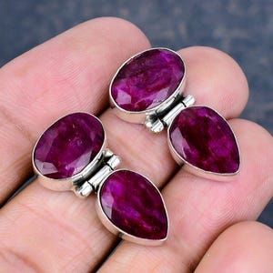 May include: Four pieces of jewelry with oval and teardrop-shaped, faceted, deep red gemstones set in silver. The gemstones have a rich, saturated color and are mounted on silver settings with a simple, elegant design.