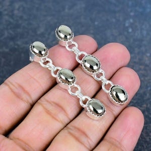 May include: Silver drop earrings with three oval, metallic-effect stones linked together. The earrings have a post-back fastening. The stones have a reflective, metallic appearance. The earrings are displayed against a neutral background.