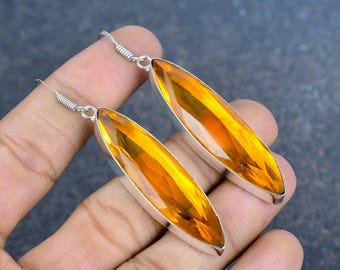 Pode incluir: Um par de brincos longos de prata com uma gema amarelo-dourado vibrante em forma de folha. Os brincos são suspensos por um gancho de prata. As pedras preciosas são facetadas, refletindo a luz.