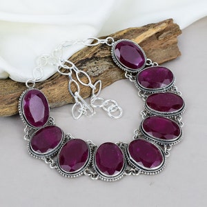 May include: A silver necklace with a chain and seven oval-shaped purple gemstones. The necklace is on a wooden surface.