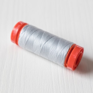 Könnte beinhalten: Eine Spule mit hellgrauem Garn und orangefarbenen Plastikenden.