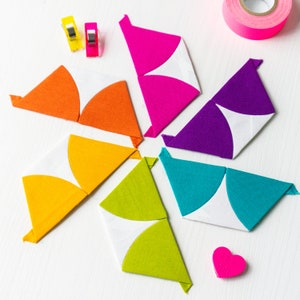 Könnte beinhalten: Sechs Stoffdreiecke in verschiedenen Farben, darunter Orange, Gelb, Grün, Blau, Lila und Pink, sind in einem Kreis angeordnet. Jedes Dreieck hat eine weiße Halbkreisform in der Mitte.