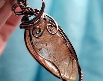 May include: A copper wire wrapped pendant featuring a clear quartz stone with golden inclusions. The wire is twisted into a decorative design.