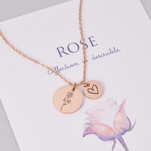 K&ouml;nnte beinhalten: Halskette aus Ros&eacute;gold mit zwei Anh&auml;ngern. Ein gro&szlig;er Kreis mit einer Rosenillustration und ein kleiner Kreis mit einem Herzen. Die Kette liegt auf einer Karte mit dem Wort "ROSE" und dem Satz "affection is desirable."
