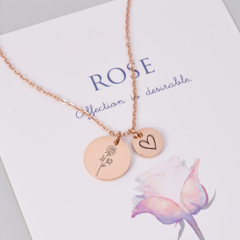K&ouml;nnte beinhalten: Halskette aus Ros&eacute;gold mit zwei Anh&auml;ngern. Ein gro&szlig;er Kreis mit einer Rosenillustration und ein kleiner Kreis mit einem Herzen. Die Kette liegt auf einer Karte mit dem Wort "ROSE" und dem Satz "affection is desirable."
