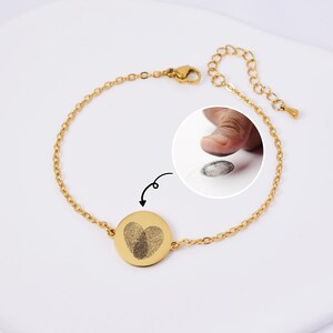 Könnte beinhalten: Goldkette Armband mit einem runden Anhänger mit einem herzförmigen Fingerabdruck-Design.