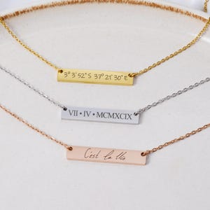 Op de afbeelding: Drie kettingen van goud, zilver en rosé goud met staafvormige hangers. De gouden hanger heeft de coördinaten "3° 3'52" S 37° 21' 30" E" gegraveerd. De zilveren hanger heeft de Romeinse cijfers "VII IV MCMXCIX" gegraveerd. De rosé gouden hanger heeft de zin "C'est la vie" gegraveerd.