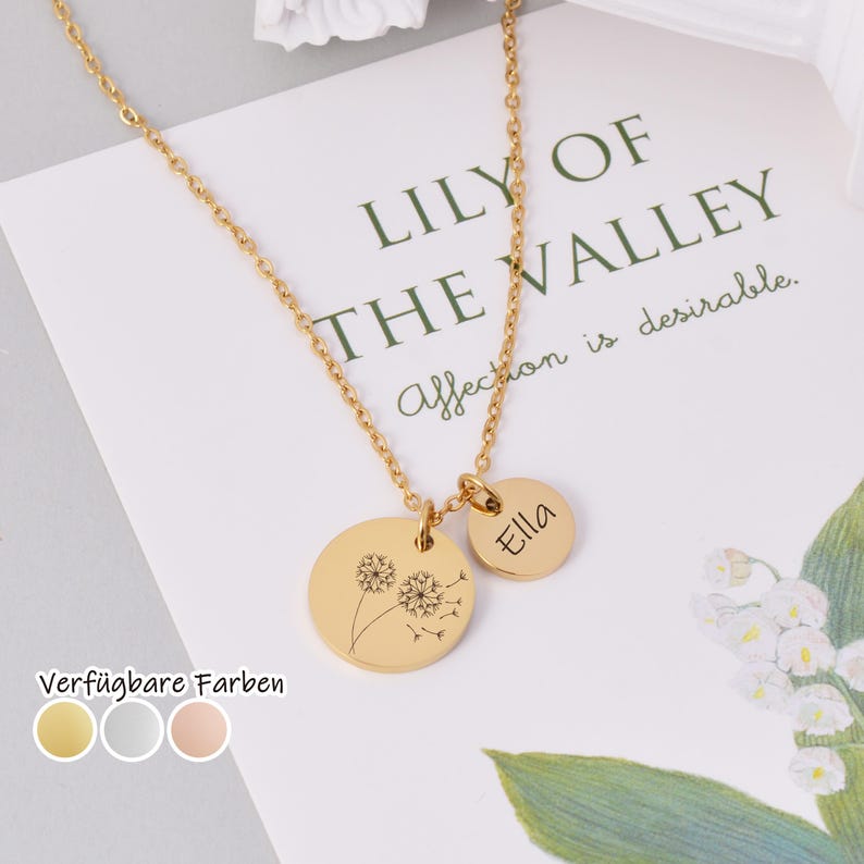 K&ouml;nnte beinhalten: Eine goldfarbene Halskette mit zwei runden Anh&auml;ngern. Ein Anh&auml;nger zeigt ein Pusteblumen-Design, der andere hat den eingravierten Namen "Ella". Die Halskette wird auf einer Karte mit dem Text "LILY OF THE VALLEY" und "Affection is desirable" pr&auml;sentiert.