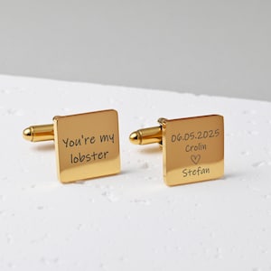 May include: A pair of gold square cufflinks. One cufflink is engraved with the text "You're my lobster". The other cufflink is engraved with the text "06.05.2025 Crolin Stefan" and a heart symbol.