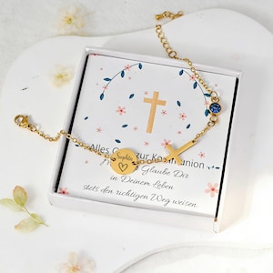 Könnte beinhalten: Goldfarbenes Armband mit Kreuz und blauem Edelstein, präsentiert in einer weißen Schachtel mit floralen Akzenten. Das Armband hat einen runden Anhänger mit Herz und dem Namen "Sophia". Die Schachtel hat deutschen Text.