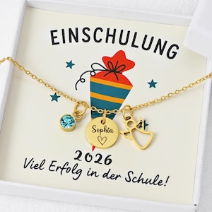 Könnte beinhalten: Goldfarbene Halskette mit drei Anhängern: einem blauen Edelstein, einem runden Anhänger mit dem Namen "Sophia" und einem Herz, sowie einem Engel. Die Kette liegt in einer weißen Box mit deutschem Text und einer Schultüten-Grafik.