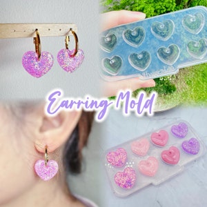 May include: A clear plastic mold for making heart-shaped earrings. The mold has eight heart-shaped cavities. The mold is filled with pink and purple glitter resin. The mold is labeled "Hygge Mom".