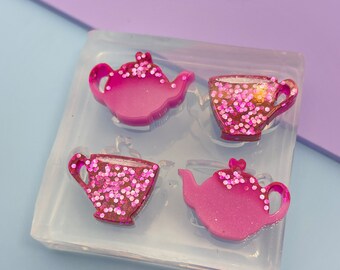 May include: A clear silicone mold with four cavities for making resin crafts. The cavities are shaped like teapots and teacups, with a pink glitter finish.