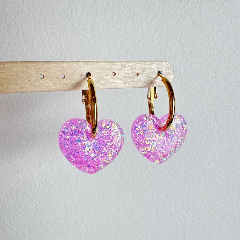 May include: A pair of gold hoop earrings with pink glitter heart charms.