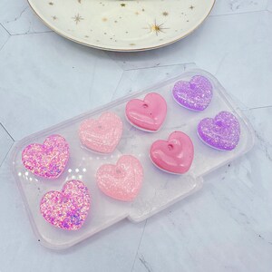 May include: A clear silicone mold with eight heart-shaped cavities. The mold is filled with pink and purple glitter hearts.