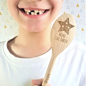 May include: A wooden spoon with a star design and the text "Mini Star Baker" and a name, "Ryan", engraved on the handle. The spoon is held by a child with a missing tooth.