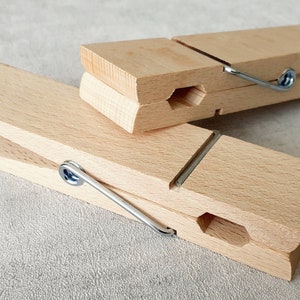 May include: Two wooden clothespins with metal springs. The clothespins are made of natural wood and have a simple design.