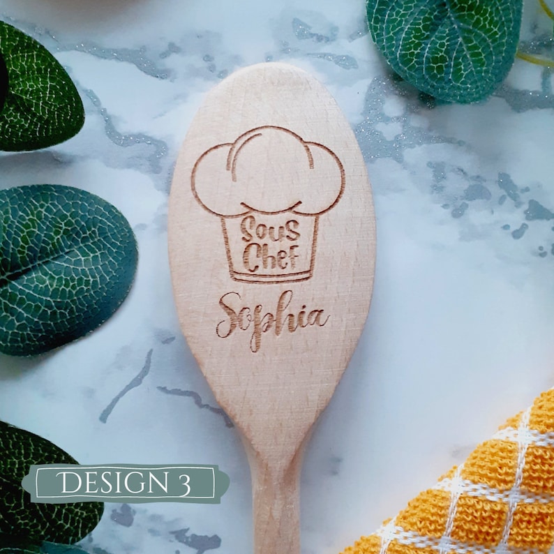 May include: A wooden spoon with the words "Sous Chef" and "Sophia" engraved on it. The spoon is decorated with a chef's hat.