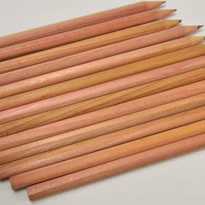 May include: A group of 15 natural wood pencils with unsharpened graphite tips. The pencils are arranged in a fan shape, with the tips pointing towards the top of the image.