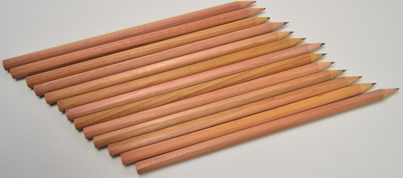 May include: A group of 15 natural wood pencils with unsharpened graphite tips. The pencils are arranged in a fan shape, with the tips pointing towards the top of the image.