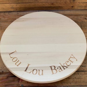 以下が含まれることがあります： 「Lou Lou Bakery」と刻まれた丸い木のケーキボードです。